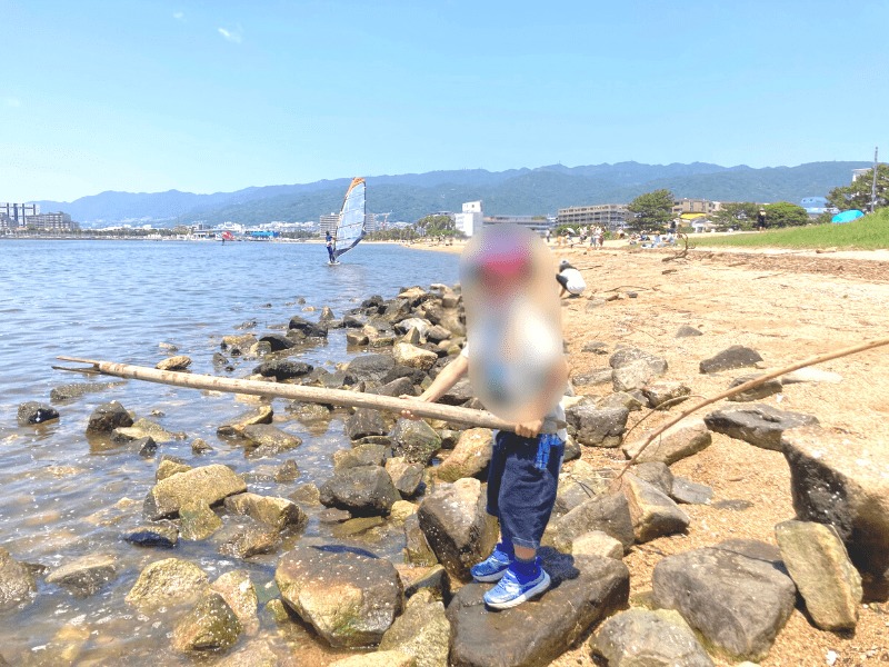 西宮市御前浜公園の砂浜の岩の上で長い棒を持って遊ぶ男の子